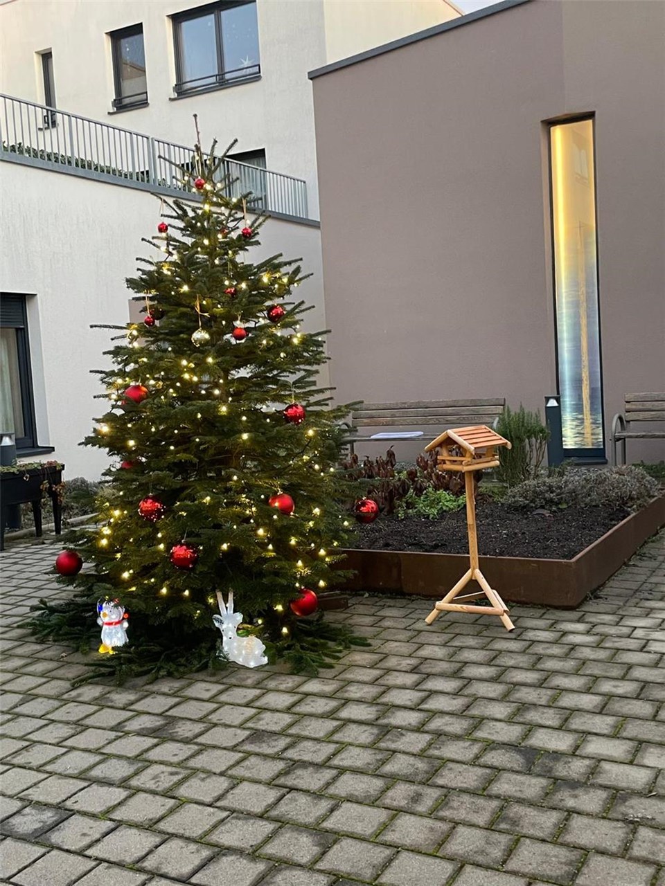 Auf dem Foto ist ein großer Weihnachtsbaum in einem Innenhof zu sehen. Geschmückt mit Lichterkette sowie roten und goldenen Kugeln.