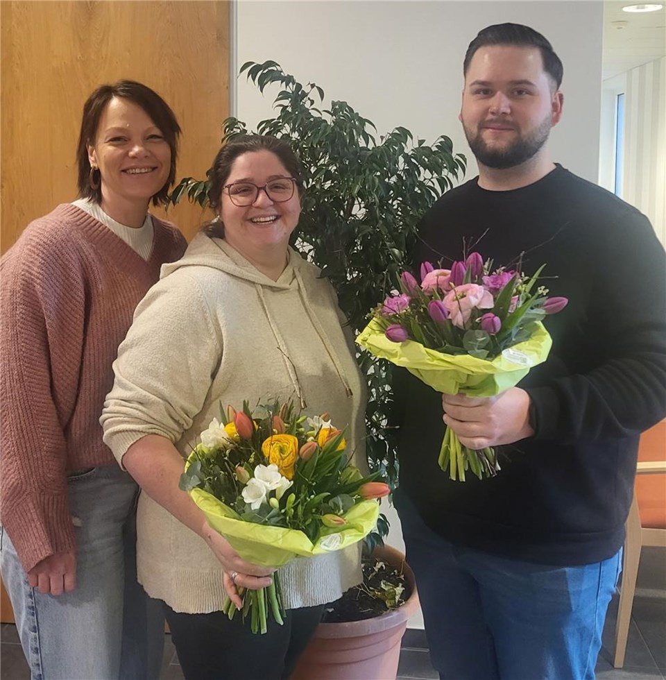 Katja Rambach, Bereichsleitung Altenhilfe mit Lena Berg und Lukas Wolfsperger, die beide einen Blumenstrauß in der Hand halten.