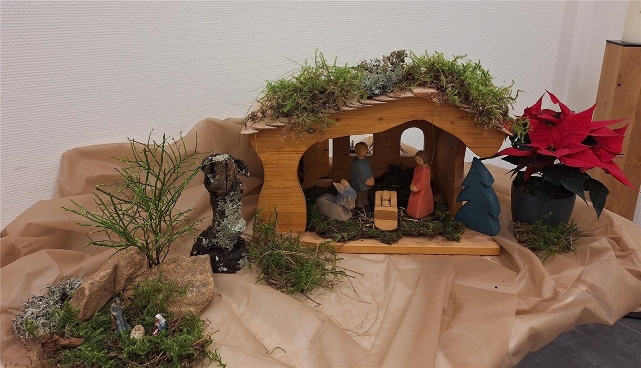 Auf dem Bild ist eine Holzkrippe mit Jesus, Maria und Josef und einem Esel zu sehen.
