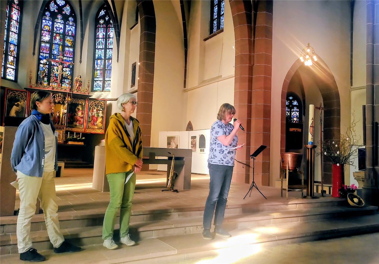 3 Personen stehen im Altarraum einer Kirche und tragen etwas vor