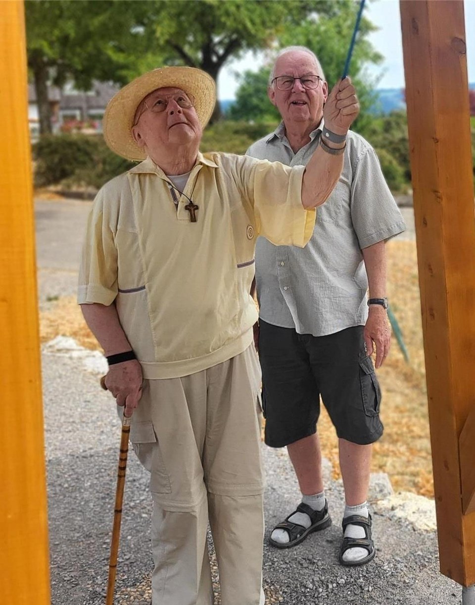 Pfarrer Engler steht an einem kleinen Holzturm, der als Aufhängung für Friedenglocke dient und läutet diese.