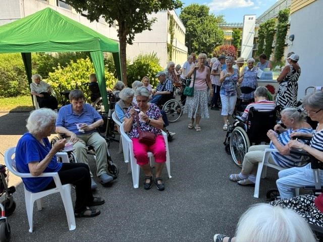 Eine Gruppe von Senior*innen, die sitzend und stehend Eis essen, im Hintergrund ist der Eiswagen zu sehen.