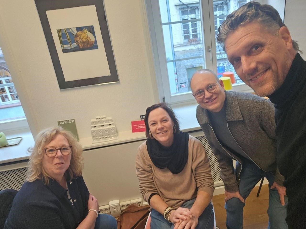 Das Bild zeigt das Leitungsteam von links Birgitt Reisenweber und Katja Rambach (sitzend) sowie Rainer Leweling und Oliver Dorgerloh stehend. Im Hintergrund sind zwei Fenster, den eine Blick in die Freiburger Altstadt gewähren