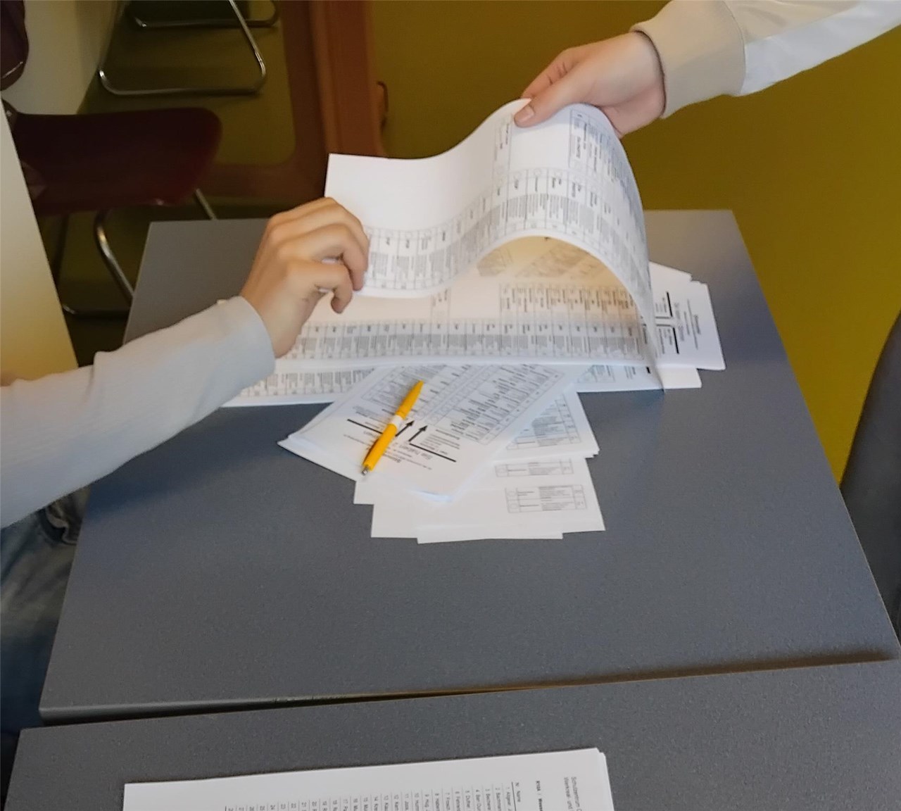 Eine Hand reicht einen Wahlzettel, eine andere Hand nimmt diesen entgegen.