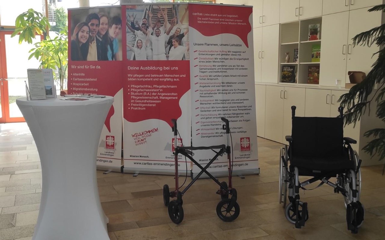 Das Foto zeigt das Foyer des Seniorenzentrums Bürkle-Bleiche mit 2 Roll-Ups mit Infos zum Caritasverband, einem Stehtisch mit Flyer und Infomaterial und einem Rollator sowie einem Rollstuhl.